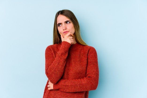 Jeune femme caucasienne isolée sur la pensée bleue et levant les yeux, réfléchissant, contemplant, ayant un fantasme.