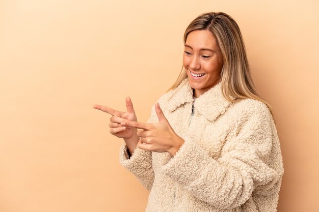 Jeune femme caucasienne isolée sur des points de fond beige avec le pouce loin, riant et insouciant.