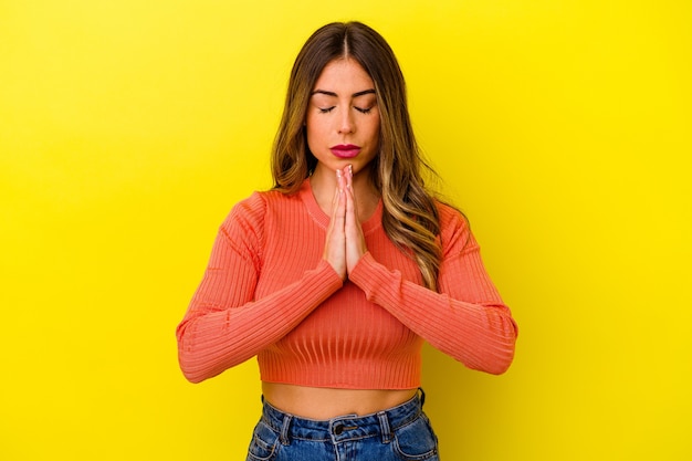 Jeune femme caucasienne isolée sur la prière jaune, montrant la dévotion, personne religieuse à la recherche d'inspiration divine.