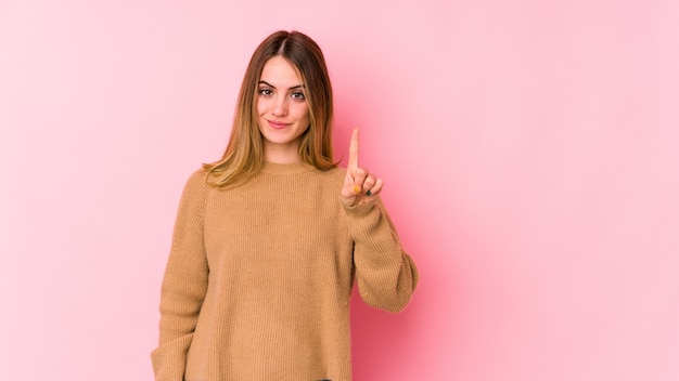 Jeune femme caucasienne isolée sur rose montrant le numéro un avec le doigt.