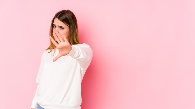 Jeune femme caucasienne isolée sur rose rejetant quelqu'un montrant un geste de dégoût.