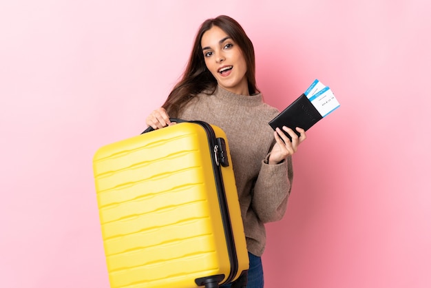 Jeune femme caucasienne isolée sur rose en vacances avec valise et passeport