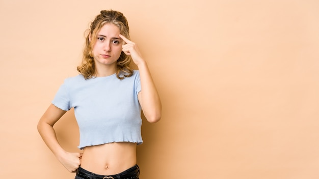 Jeune femme caucasienne isolée sur le temple de pointage beige avec le doigt, la pensée, concentrée sur une tâche.