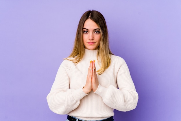 Jeune femme caucasienne isolée sur violet priant, montrant la dévotion, la personne religieuse à la recherche d'inspiration divine.