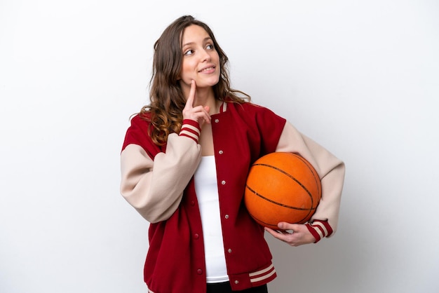 Jeune femme caucasienne jouant au basket isolé sur fond blanc en pensant à une idée tout en levant les yeux