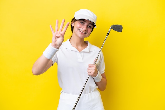 Jeune femme caucasienne jouant au golf isolé sur fond jaune heureux et comptant quatre avec les doigts