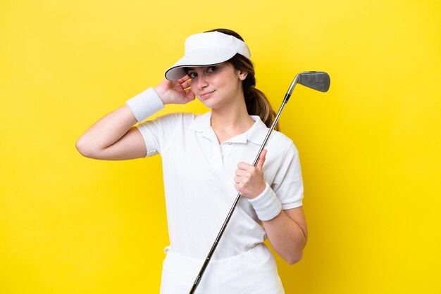 Jeune femme caucasienne jouant au golf isolée sur fond jaune ayant des doutes