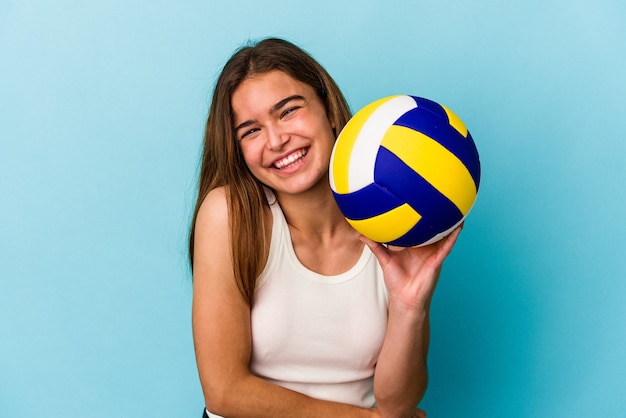 Jeune femme caucasienne jouant au volley-ball isolé sur fond bleu en riant et en s'amusant.