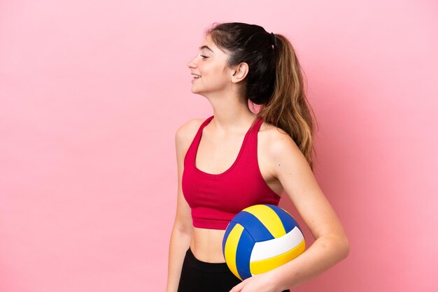 Jeune femme caucasienne jouant au volley-ball isolé sur fond rose en riant en position latérale