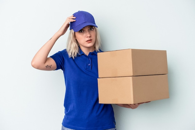 Jeune femme caucasienne de livraison isolée sur fond bleu étant choquée, elle s'est souvenue d'une réunion importante.