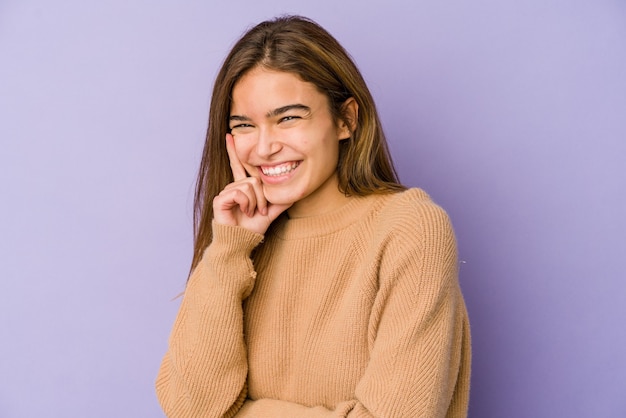 Jeune femme caucasienne maigre sur violet souriant heureux et confiant, touchant le menton avec la main.