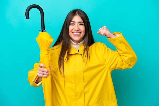 Jeune femme caucasienne avec manteau imperméable et parapluie isolé sur fond bleu faisant un geste fort