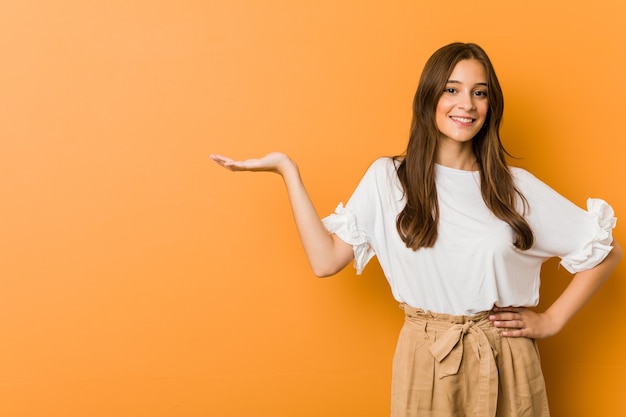 Jeune femme caucasienne montrant un espace de copie sur une paume et tenant une autre main sur la taille.