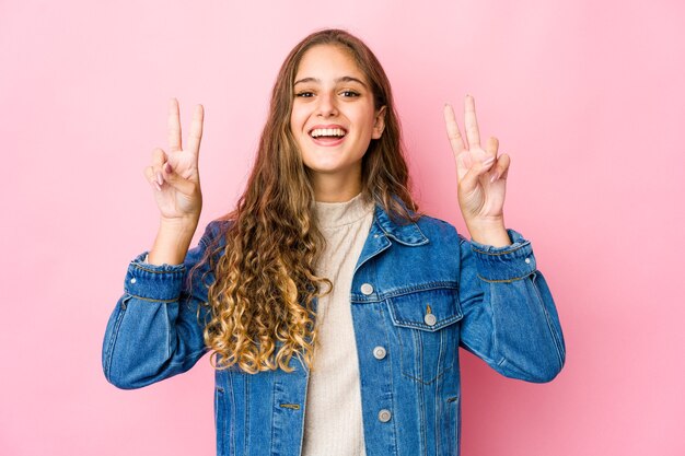 Jeune femme caucasienne montrant le signe de la victoire et souriant largement.