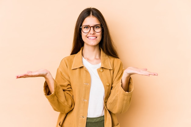 Jeune femme caucasienne sur mur beige fait l'échelle avec les bras, se sent heureuse et confiante.