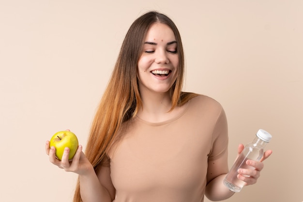 Jeune femme caucasienne sur mur beige avec une pomme et avec une bouteille d'eau