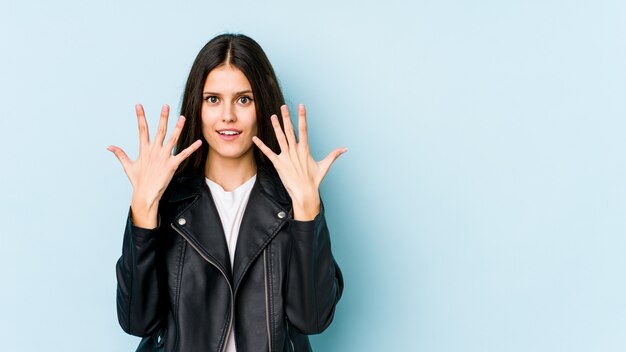 Jeune femme caucasienne sur mur bleu montrant le numéro dix avec les mains.