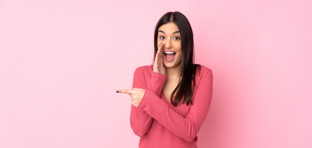 Jeune femme caucasienne sur mur pointant vers le côté pour présenter un produit et chuchoter quelque chose