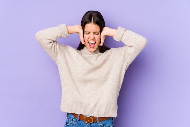 Jeune femme caucasienne sur mur violet couvrant les oreilles avec les mains essayant de ne pas entendre un son trop fort