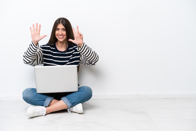 Jeune femme caucasienne avec un ordinateur portable assis sur le sol isolé sur fond blanc en comptant huit avec les doigts