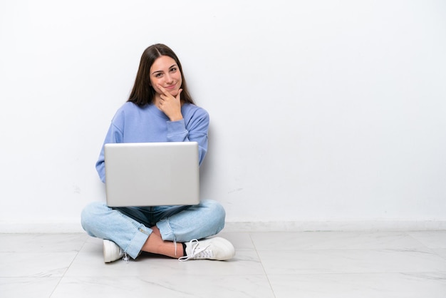 Jeune femme caucasienne avec ordinateur portable assis sur le sol isolé sur fond blanc souriant