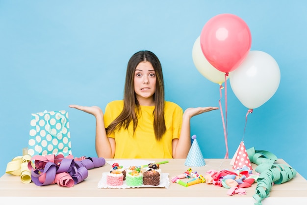 Jeune femme caucasienne organisant un anniversaire confus et douteux en haussant les épaules pour tenir un espace de copie.