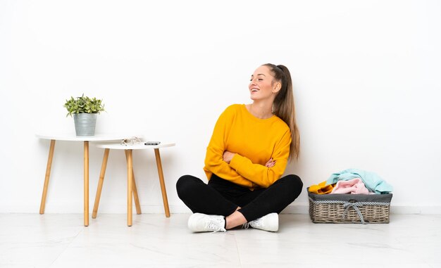 Jeune femme caucasienne pliant des vêtements assis sur le sol isolé sur fond blanc heureux et souriant