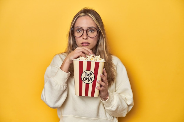 Jeune femme caucasienne pop-corn à la main exprimant son amour pour le cinéma sur fond jaune