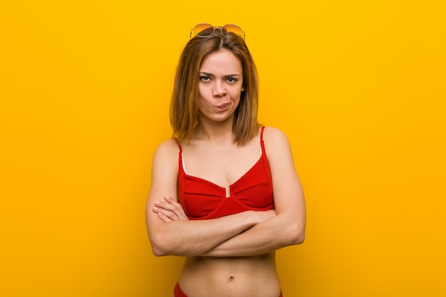 Jeune femme caucasienne portant bikini et lunettes de soleil malheureux à la recherche à huis clos avec une expression sarcastique.