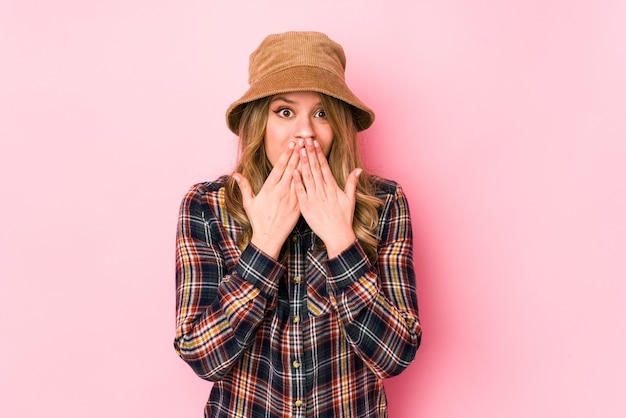 Jeune femme caucasienne portant un chapeau isolé choqué, couvrant la bouche avec les mains