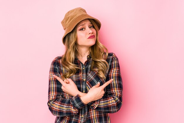 Jeune femme caucasienne portant un chapeau isolé sur le côté, essaie de choisir entre deux options.