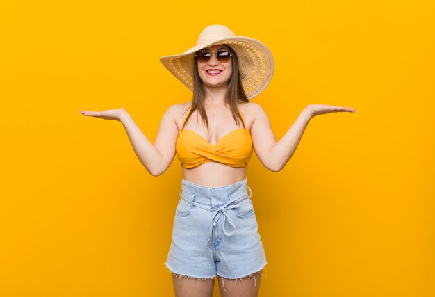 Jeune femme caucasienne portant un chapeau de paille, le look de l'été fait échelle avec les bras, se sent heureux et confiant.