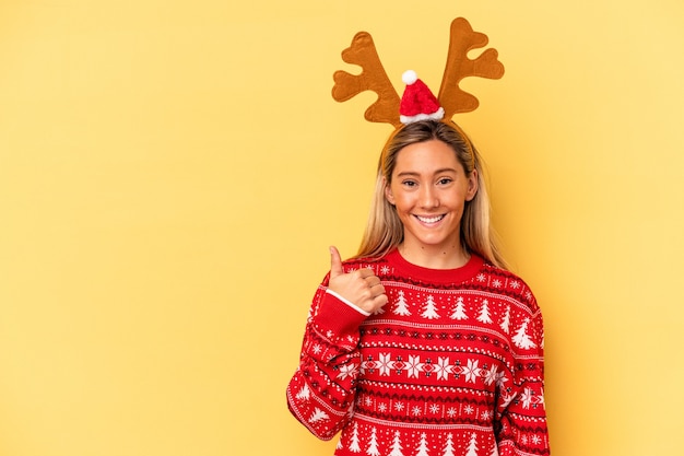 Jeune femme caucasienne portant un chapeau de renne de noël isolé sur fond beige souriant et levant le pouce vers le haut