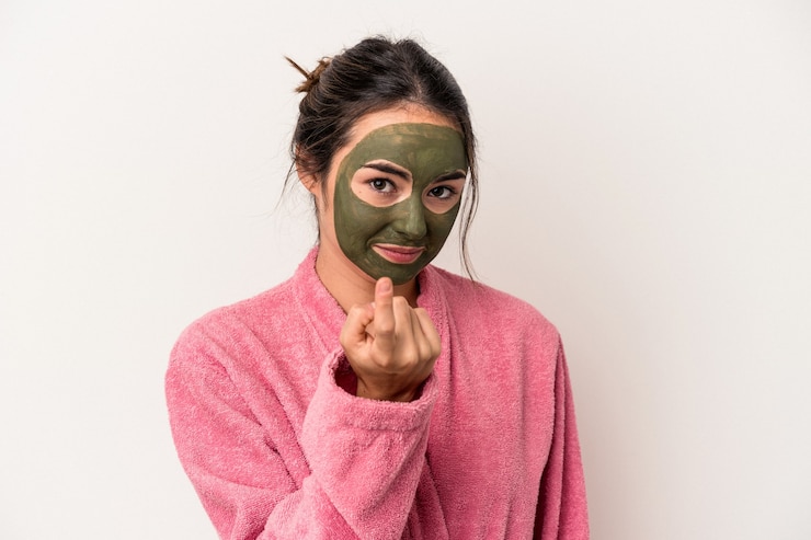 Photo jeune femme caucasienne portant un masque facial isolé sur fond blanc pointant du doigt vers vous comme si vous vous invitiez à vous rapprocher.