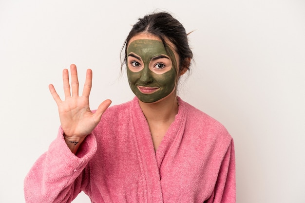 Jeune femme caucasienne portant un masque facial isolé sur fond blanc souriant joyeux montrant le numéro cinq avec les doigts.