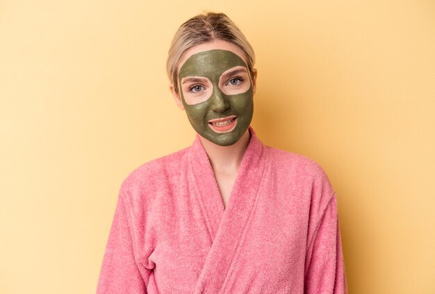 Jeune femme caucasienne portant un masque facial isolé sur fond jaune heureuse, souriante et joyeuse.