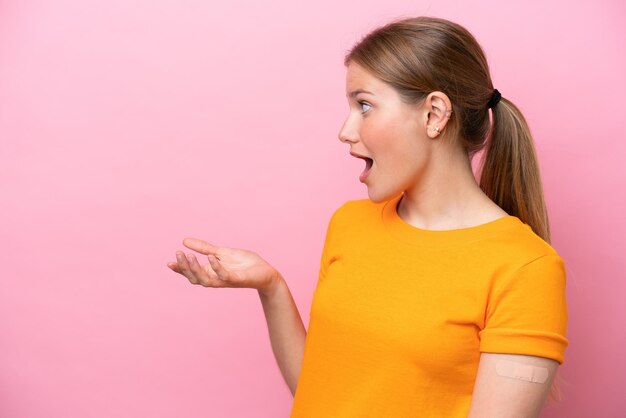 Jeune femme caucasienne portant un pansement isolé sur fond rose avec une expression faciale surprise