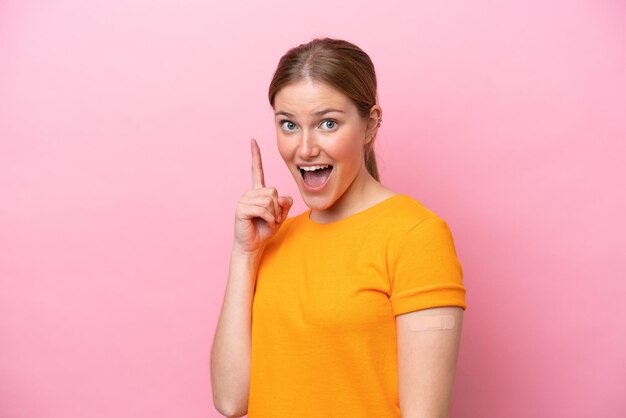 Jeune femme caucasienne portant un pansement isolé sur fond rose pointant vers le haut une excellente idée