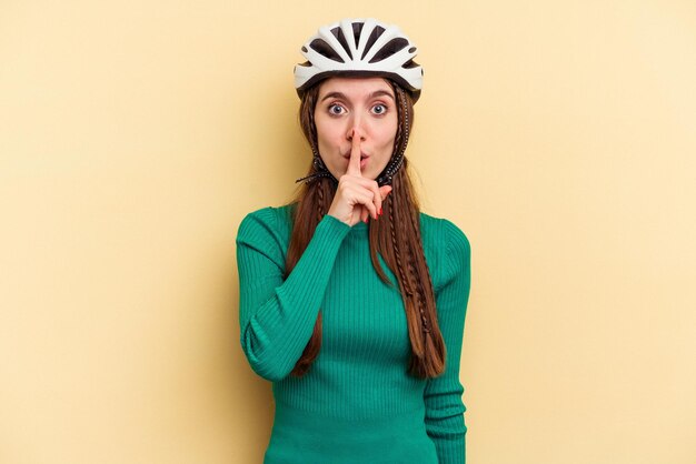 Jeune femme caucasienne portant un vélo casque isolé sur fond jaune gardant un secret ou demandant le silence.