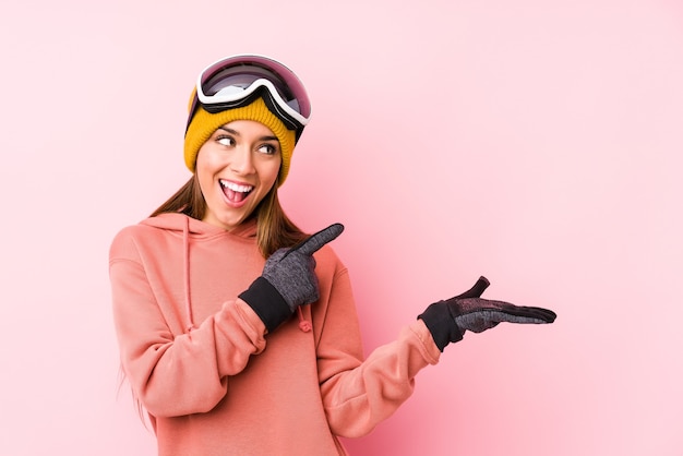 Photo jeune femme caucasienne portant un vêtement de ski isolé excité tenant un espace de copie sur la paume.