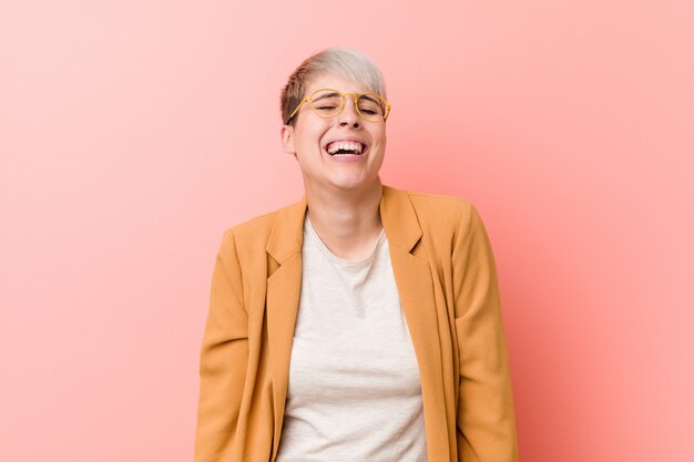 Jeune femme caucasienne portant un vêtement de travail décontracté rit et ferme les yeux, se sent détendue et heureuse.