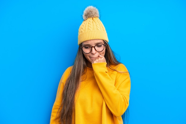 Jeune femme caucasienne portant des vêtements d'hiver isolés sur fond bleu ayant des doutes