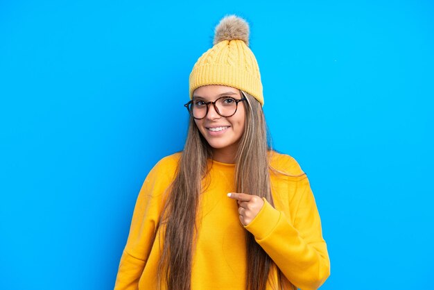 Jeune femme caucasienne portant des vêtements d'hiver isolés sur fond bleu avec une expression faciale surprise