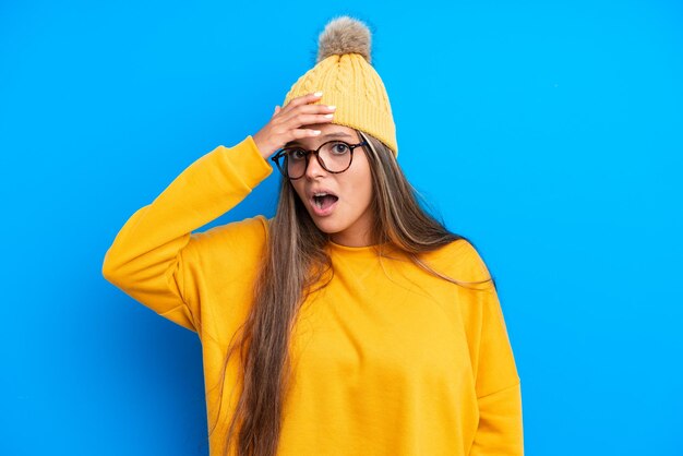 Jeune femme caucasienne portant des vêtements d'hiver isolés sur fond bleu faisant un geste de surprise tout en regardant sur le côté