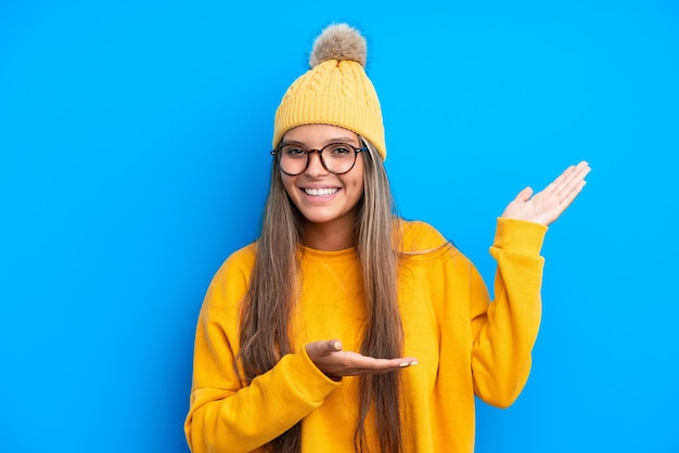 Jeune femme caucasienne portant des vêtements d'hiver isolés sur fond bleu tendant les mains sur le côté pour inviter à venir