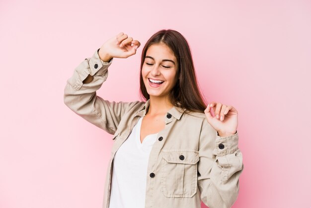 Jeune femme caucasienne posant dans un mur rose célébrant une journée spéciale, saute et lève les bras avec énergie.