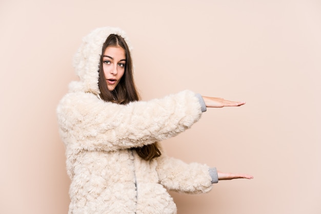 Jeune femme caucasienne posant isolé choqué et étonné tenant un espace de copie entre les mains.