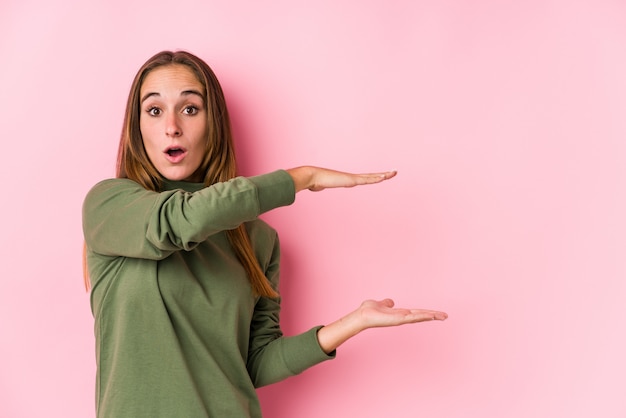 Jeune femme caucasienne posant isolé choqué et étonné tenant un espace de copie entre les mains.