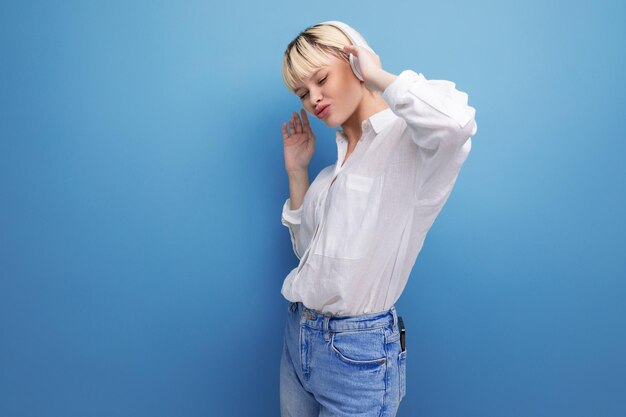 Jeune femme caucasienne positive avec une coupe de cheveux courte vêtue d'une chemise blanche et d'un jean utilise le sans fil