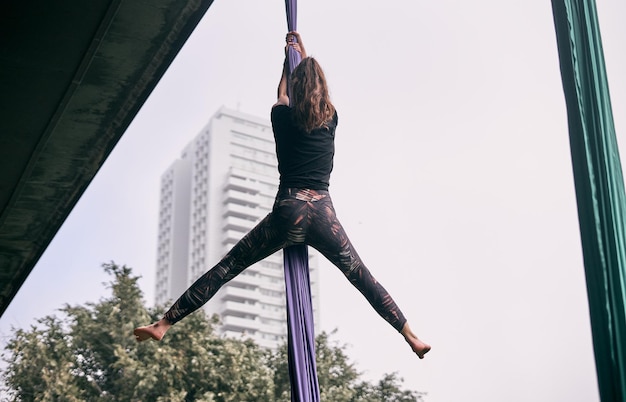 Une jeune femme caucasienne pratiquant une performance de soie aérienne accrochée à un pont dans une ville de parc